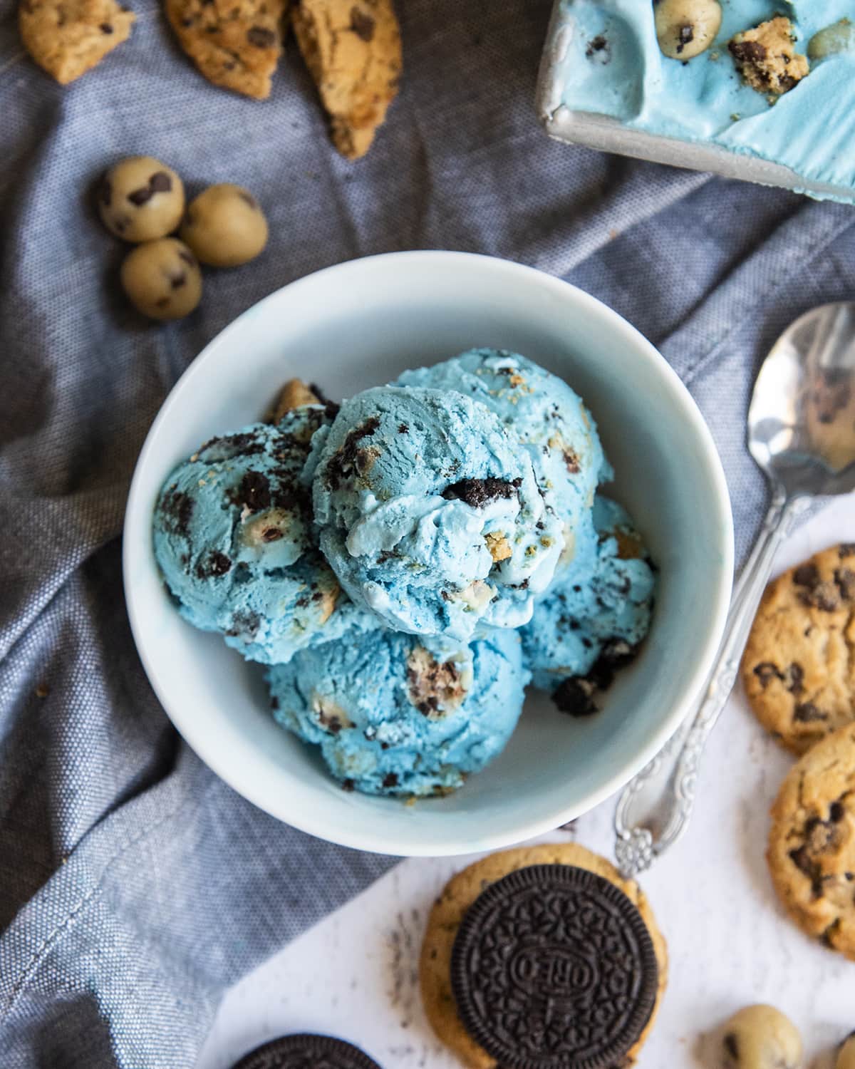 Aerial shot of a blue cookie monster bowl full of Oreos, cookies and cookie dough. Surrounded by ahoy cookies and Oreo cookies.