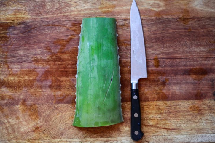 A piece of aloe vera leaf on a cutting board next to a knife.