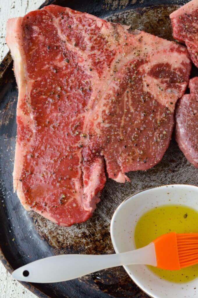 A small white bowl holds a piece of blue cheese and 2 halves of a stick of butter. This dish sits next to a pan where you can see a portion of the bone-in steak.