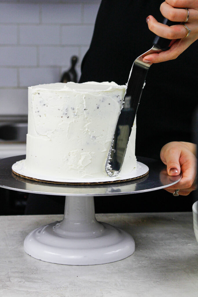 image of purple frosting being smoothed onto a cake with a bench scraper to show how to Frost a Cake Smoothly