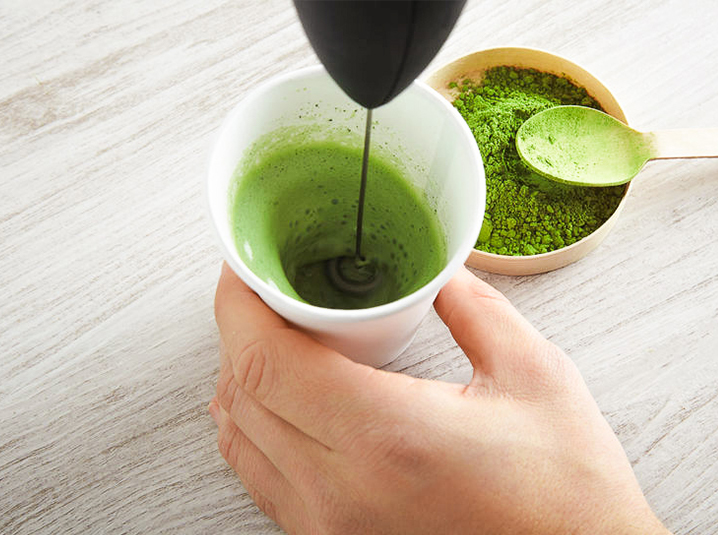 blender to puree matcha in white cup with matcha powder and teaspoon on the side
