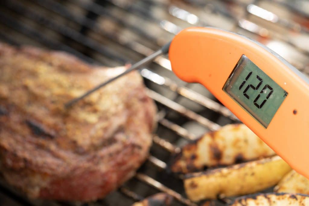 An orange thermometer records a temperature of 120 degrees F inside the steak.