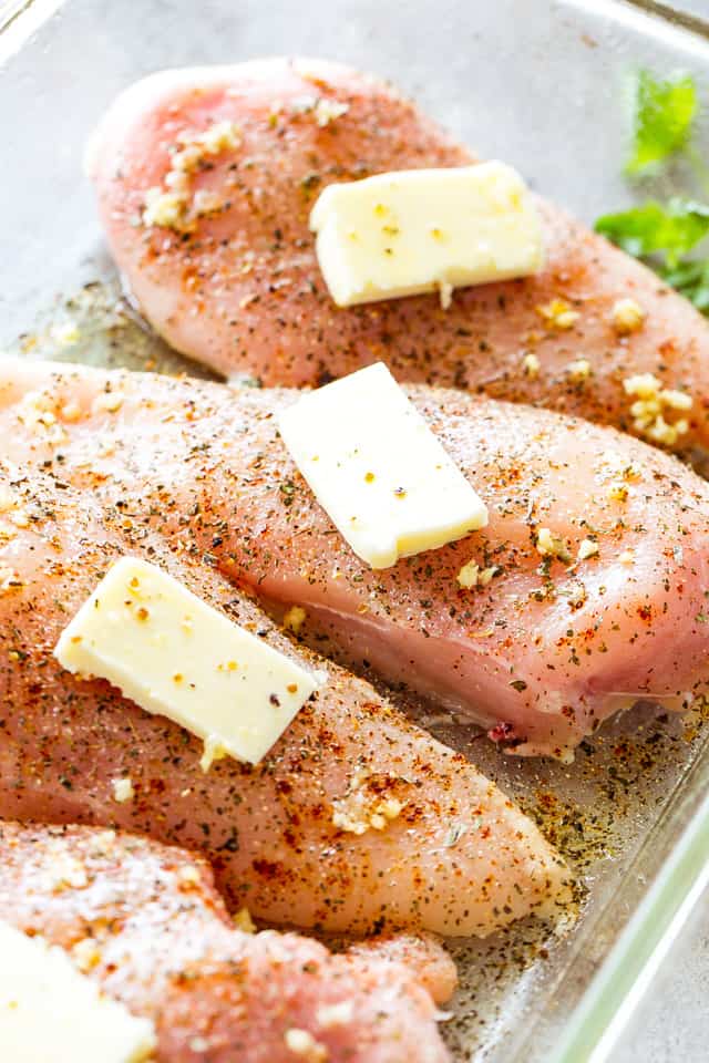 Raw chicken in a baking dish with a layer of butter on each chicken breast.
