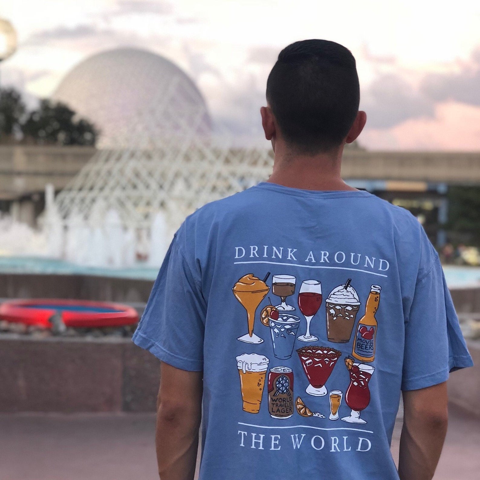 man wearing drink around the world shirt at epcot looking at a fountain at sunset