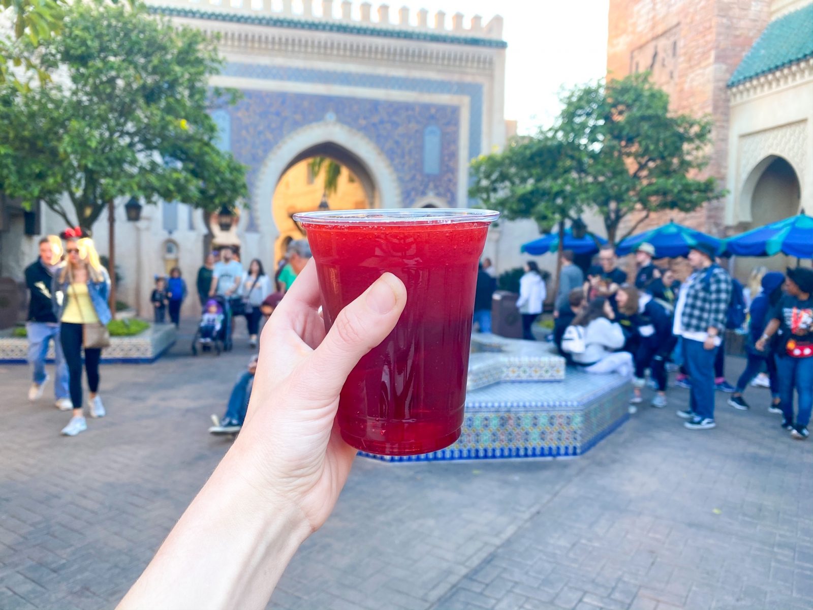 hand holding up Habibi daiquiri in Morocco Epcot with people and a fountain in the background