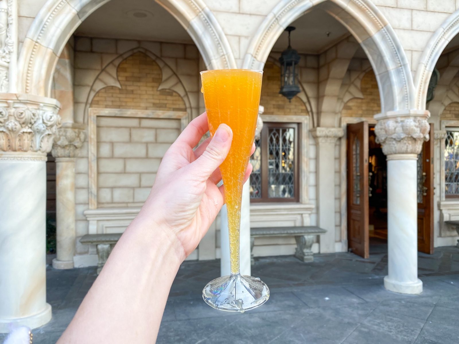 hand holding up a bellini against italian architecture while drinking around the world at disney