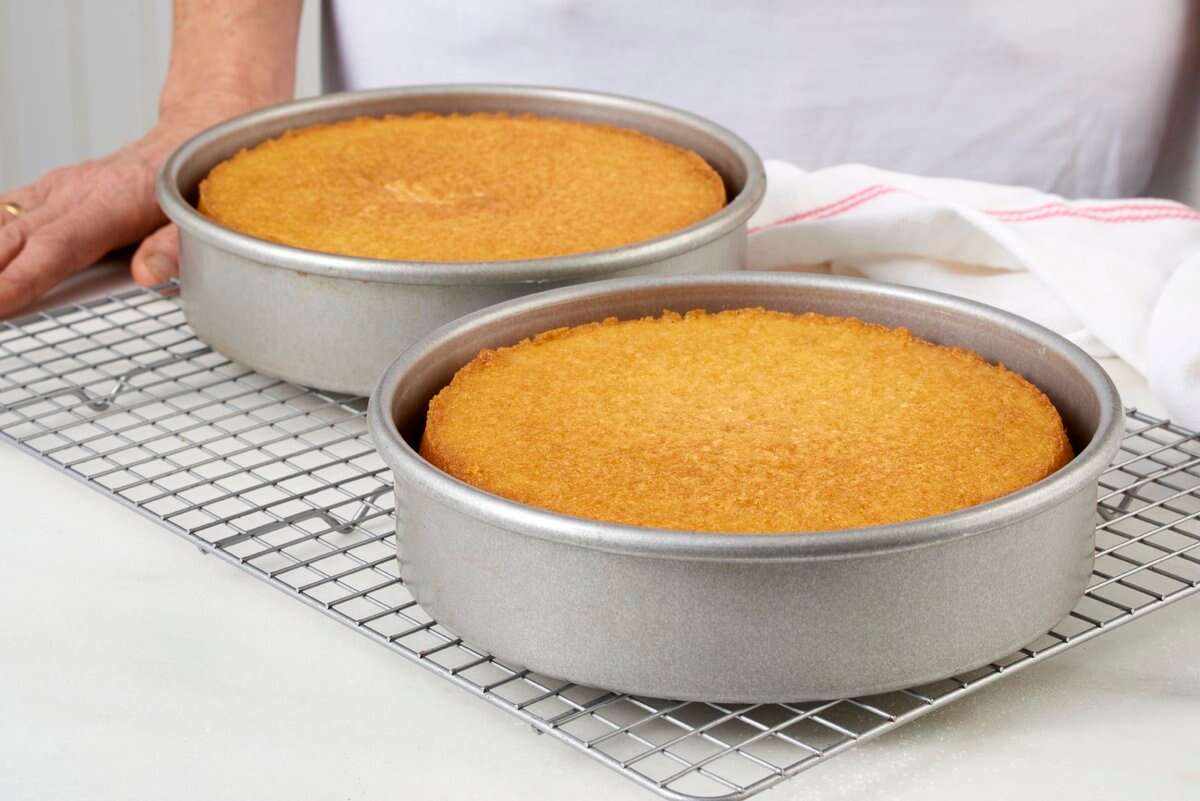Two round cake pans coated with vanilla on a cooling rack are golden brown