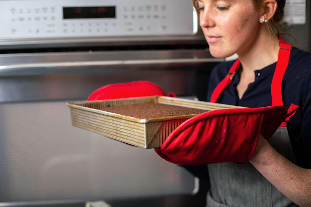 A baker is smelling freshly baked chocolate cake in front of the oven