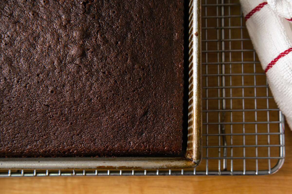 A chocolate cake pan on a cooling rack with a small gap between the sides of the pan and the cake