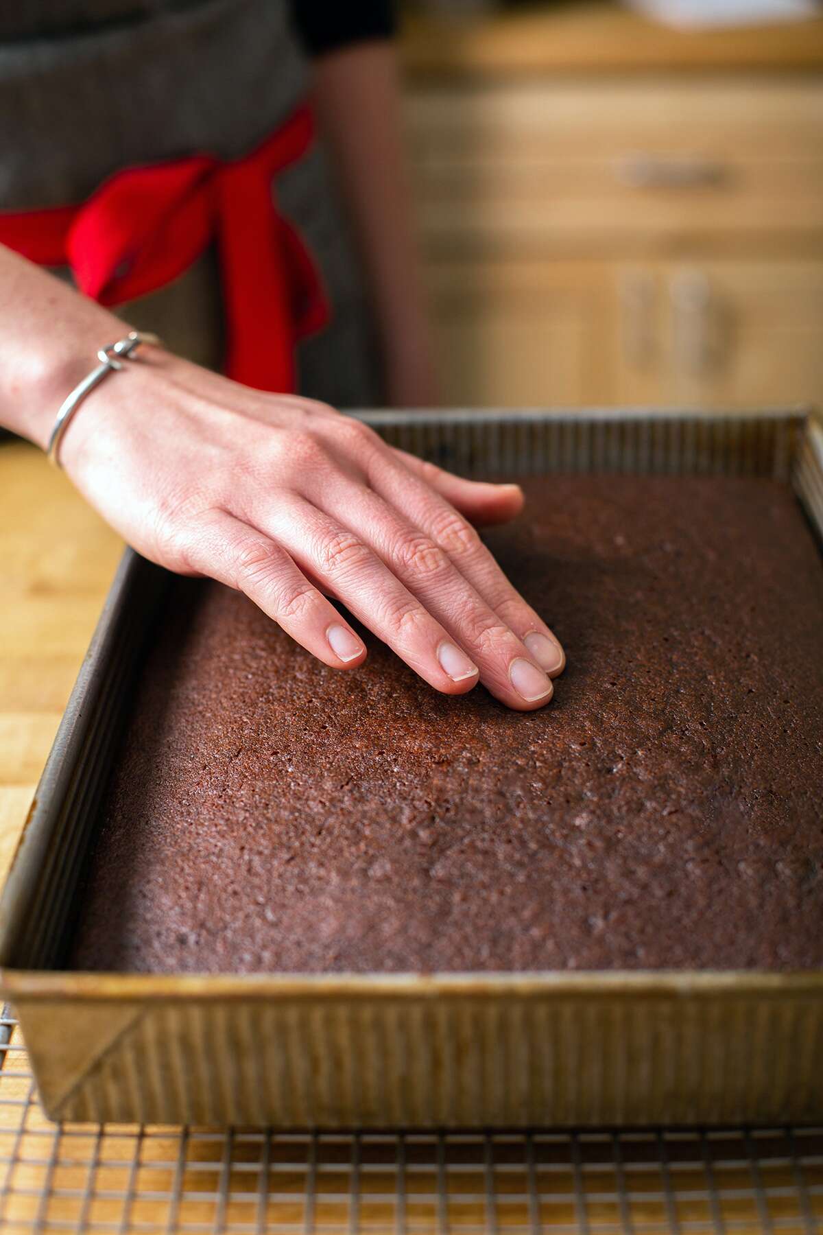 A baker presses on the center of a chocolate cake to see if it has