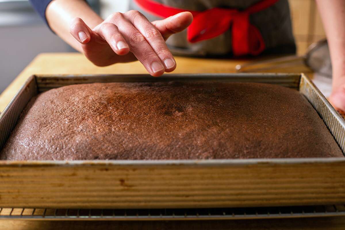 A baker presses the center of a chocolate cake
