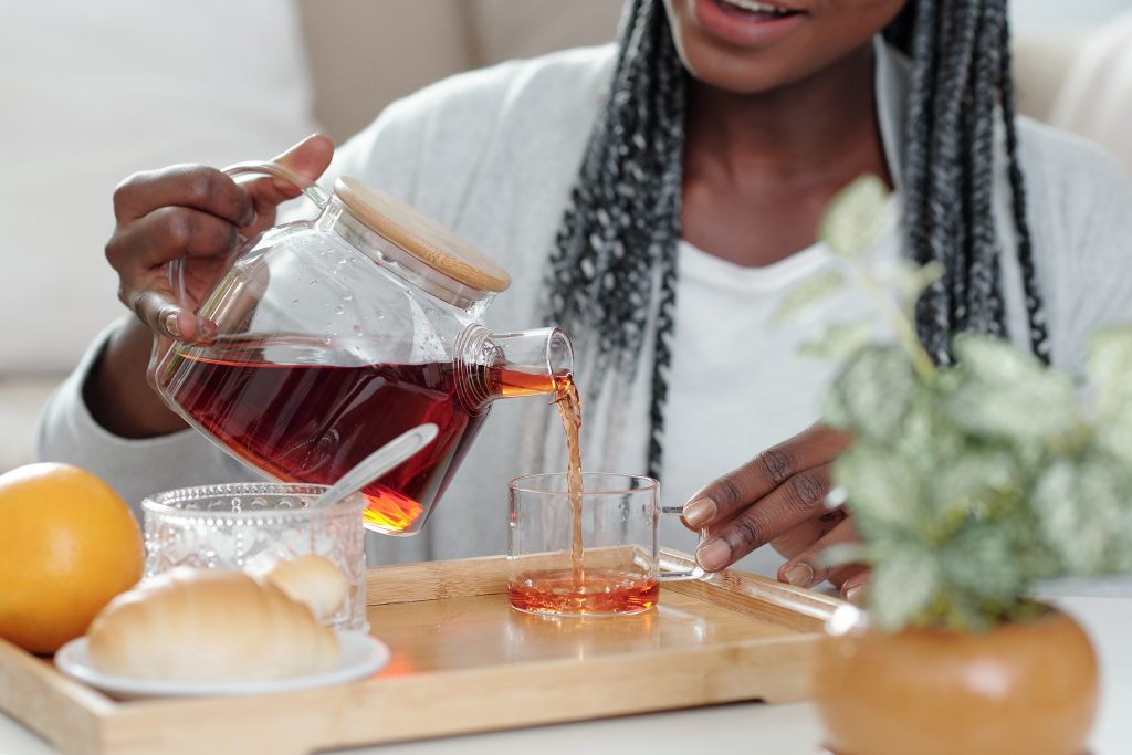 A black woman makes herself a cup of hot tea at home.