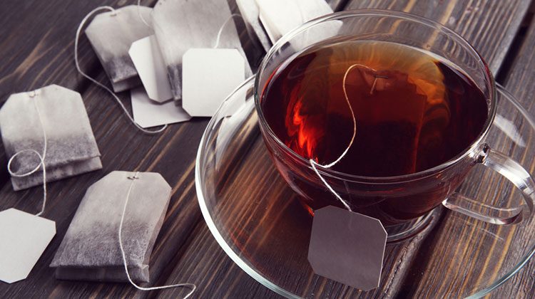 Glass cup filled with tea surrounded by tea bags on wooden table top
