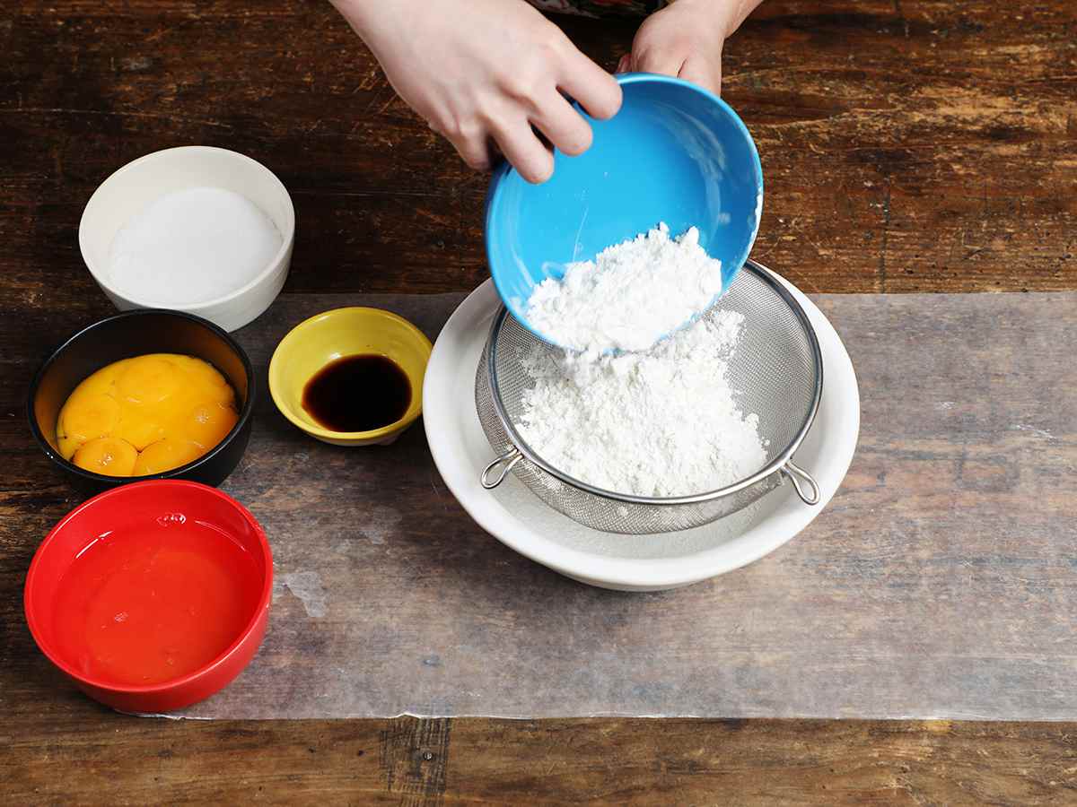 Pouring flour from blue bowl into mesh strainer