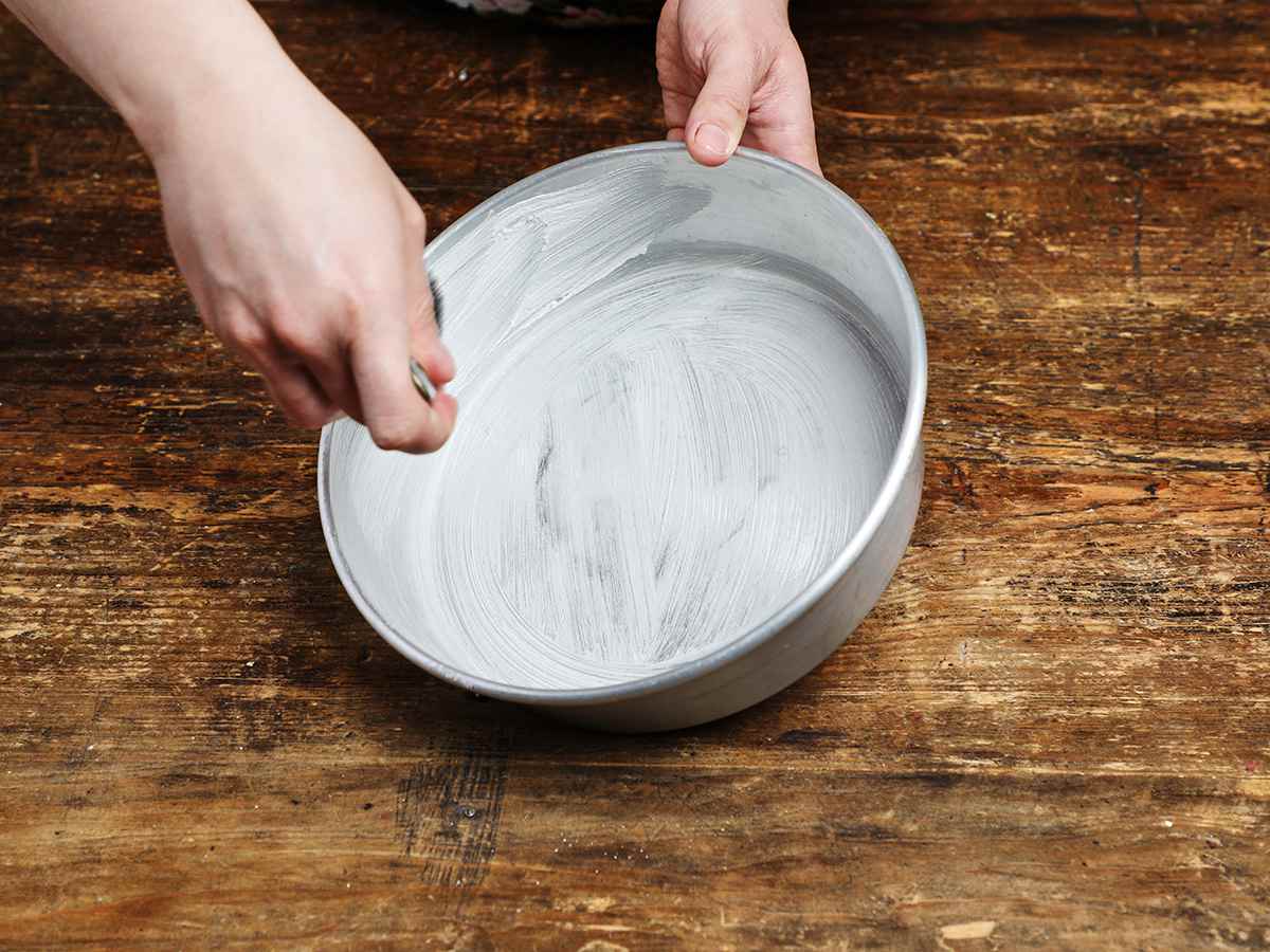Buttering round cake pan with pastry brush
