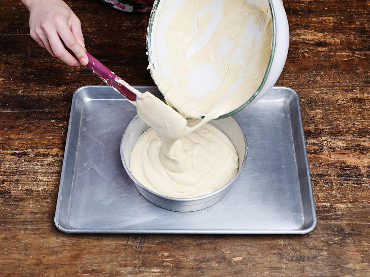 Scraping tres leches batter into cake pan with spatula