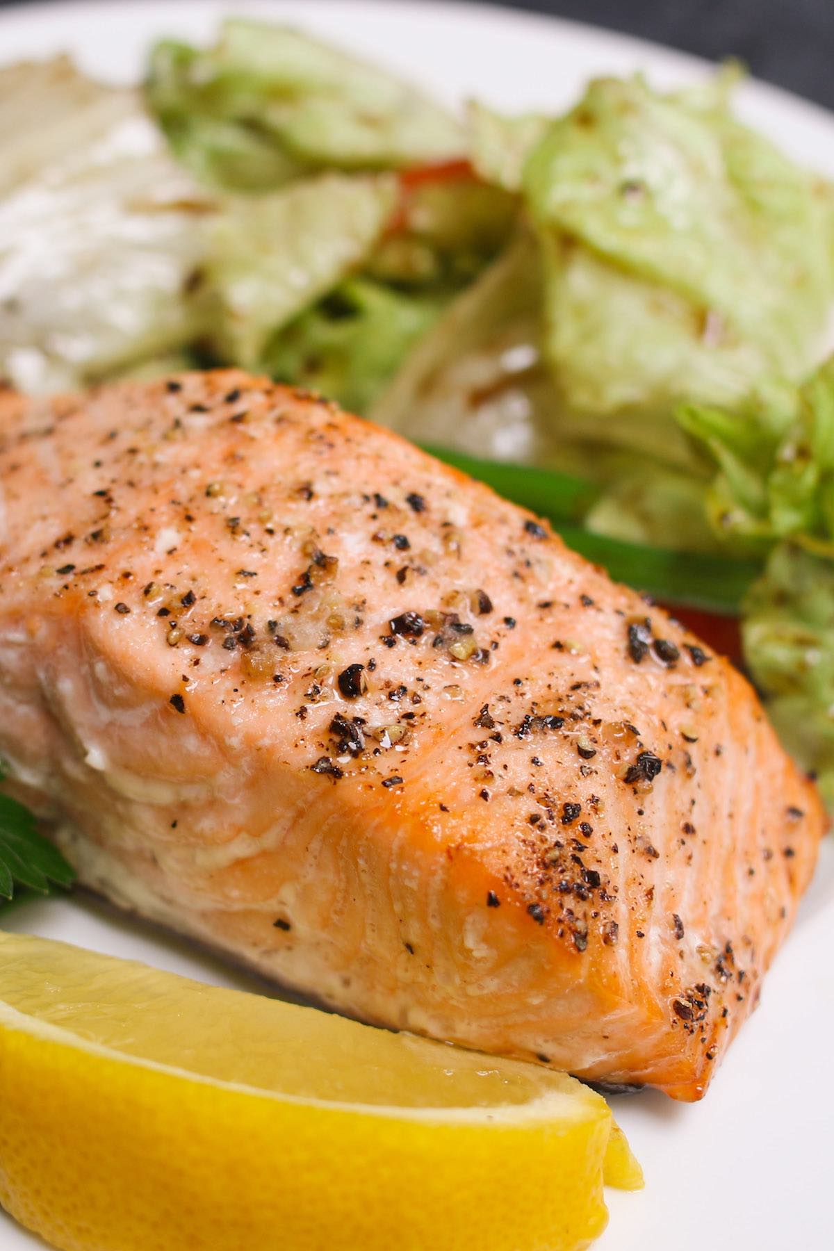 Serve portion grilled salmon fillet with a side salad on a serving plate with lemon