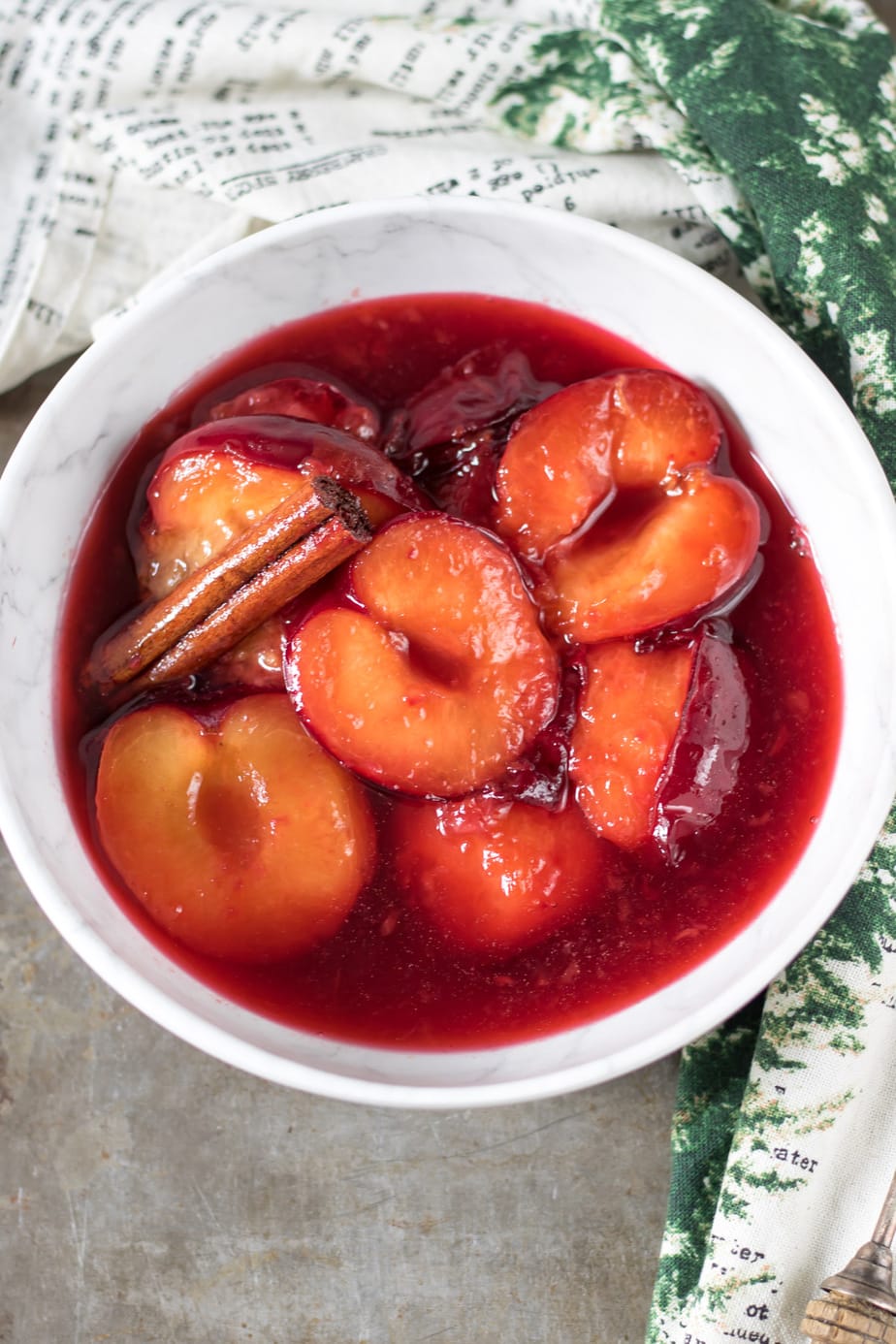 A bowl of ripe plums and a cinnamon stick.