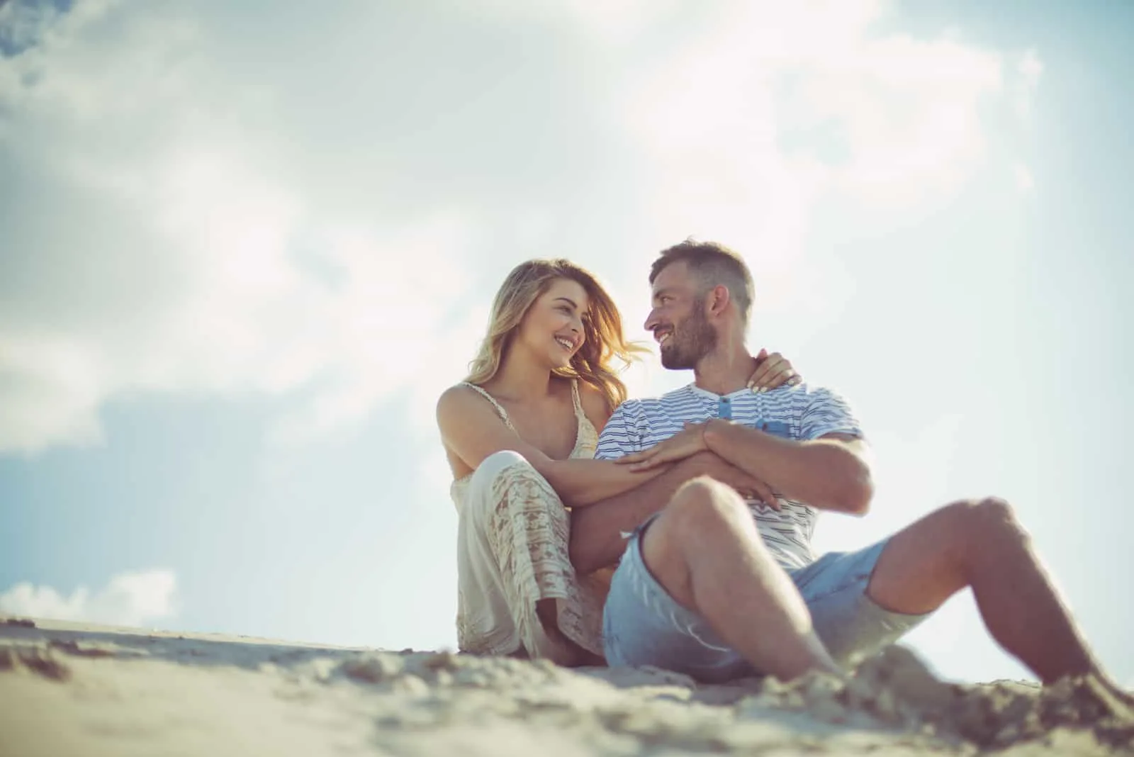 a smiling man and woman embracing sitting on the beach
