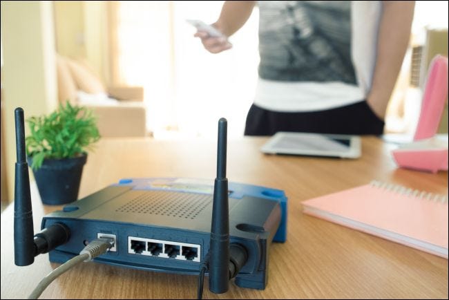 Close-up of a wireless router and a young man using a smartphone in a living room at home with a window in the back