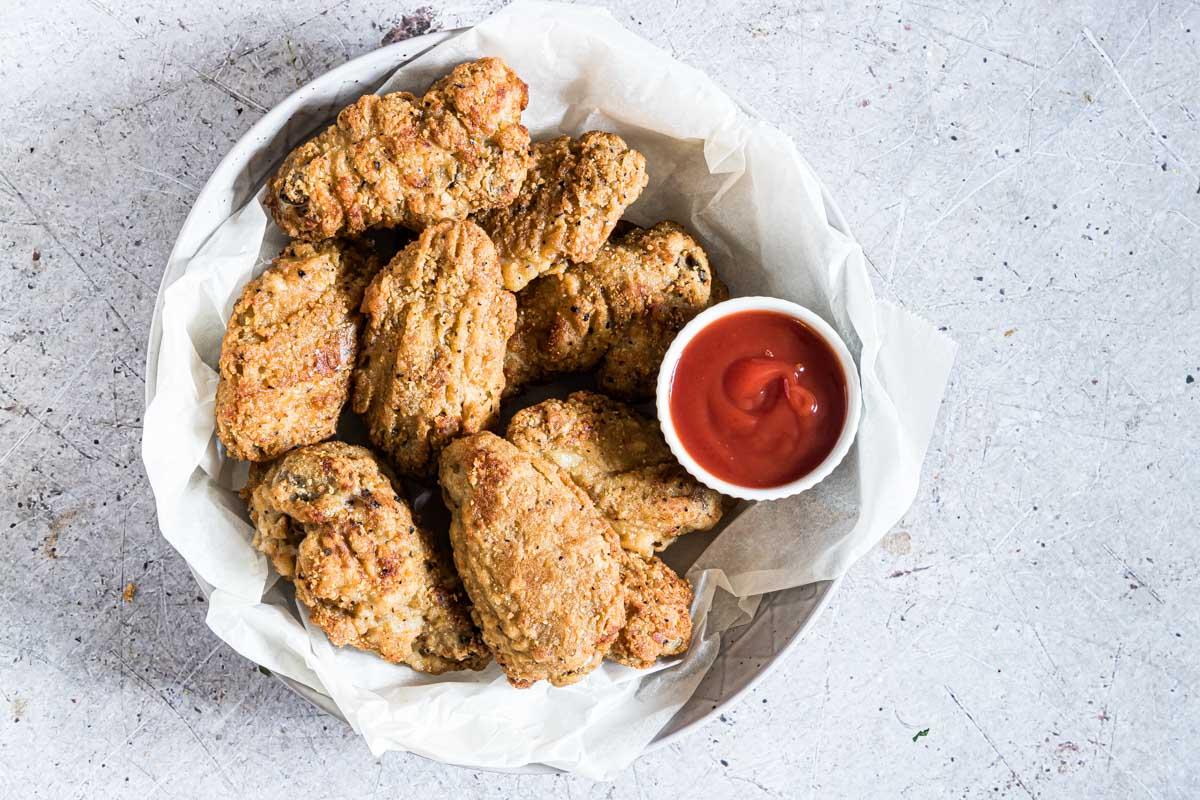 Horizontal image of a bowl of breaded chicken wings with sauce on the table