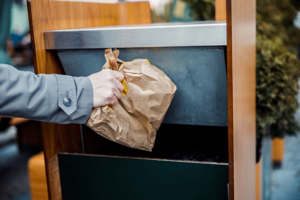 male hand throwing a crumpled fast food paper bag into a dustbin
