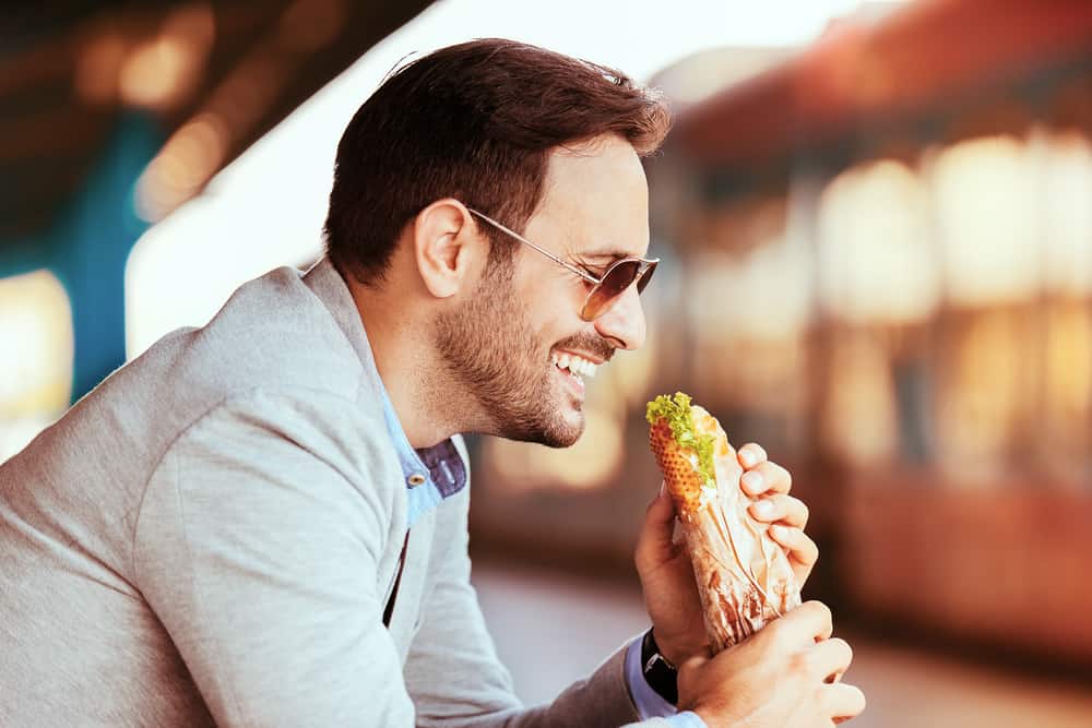 Young businessman on railroad station is eating sandwich