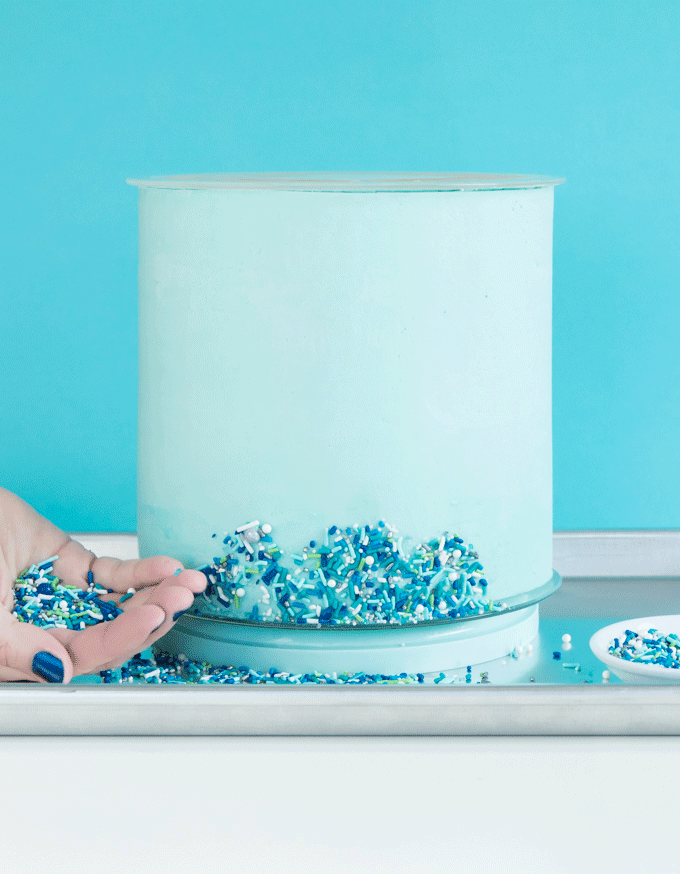 GIF about adding sprinkles to the top of a cake.