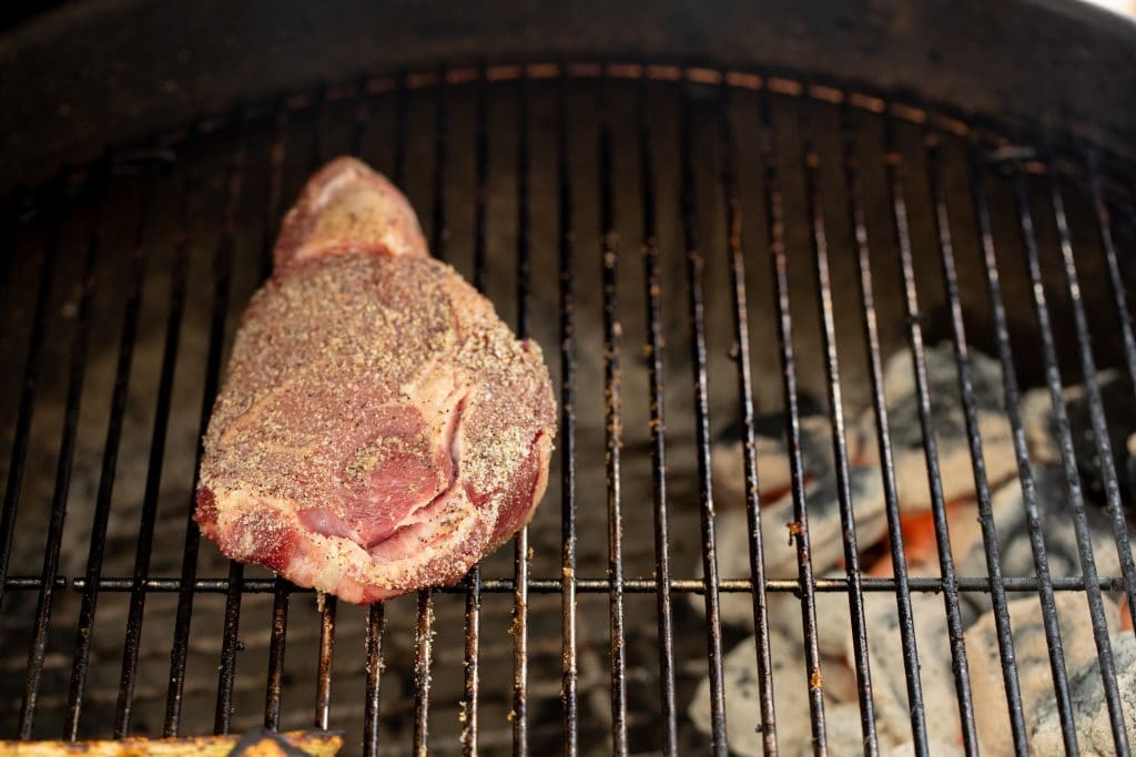 Seasoned steak on the grill with hot coals underneath the opposite side of the grill.