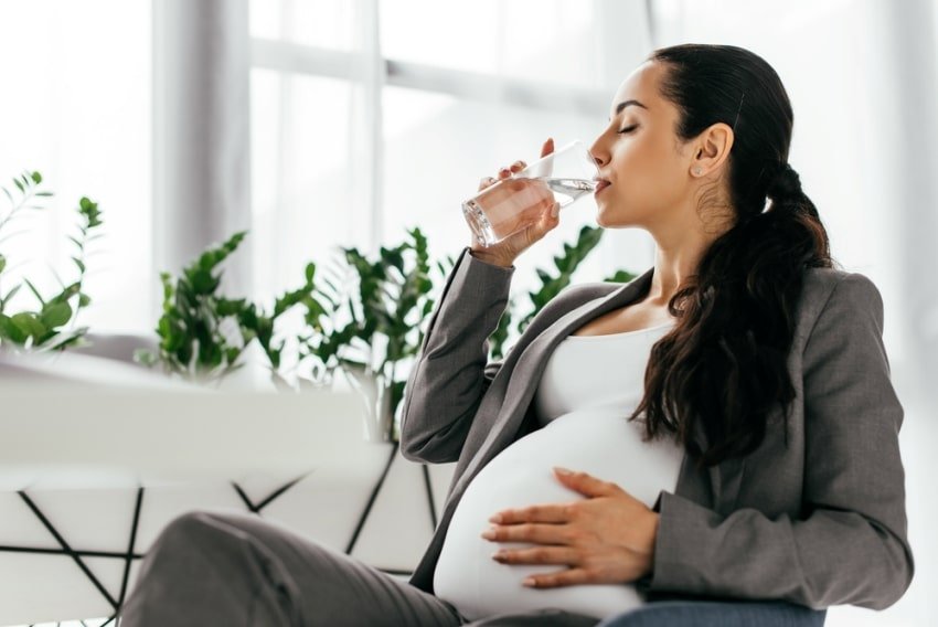 Pregnant woman sitting on office chair and drinking water