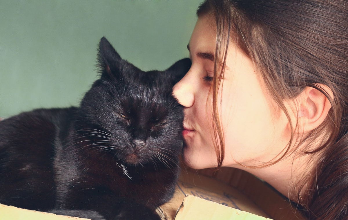 beautiful teen girl kissing black cat close-up portrait