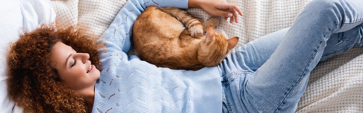 Woman lying in bed with ginger cat curled up under her arm