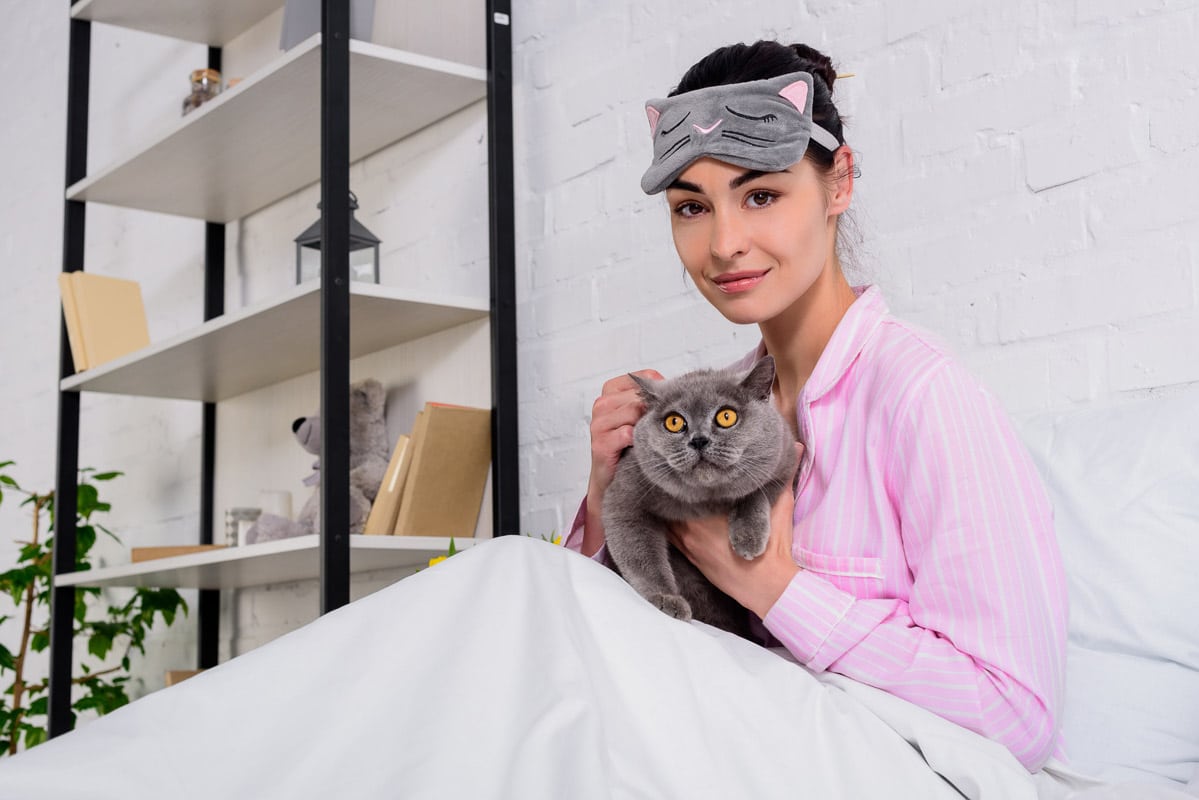woman wearing cat mask and cat in bed