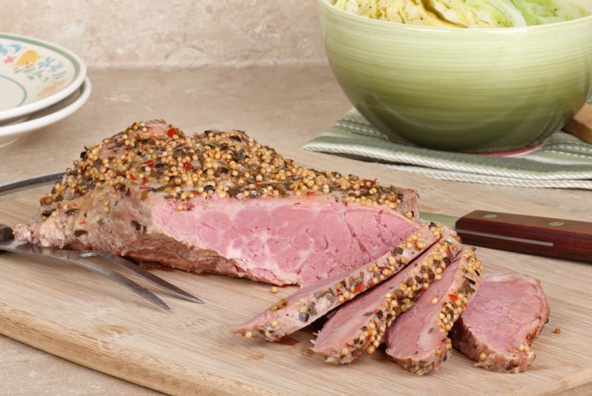 Sliced corned beef on a cutting board with a bowl of cabbage