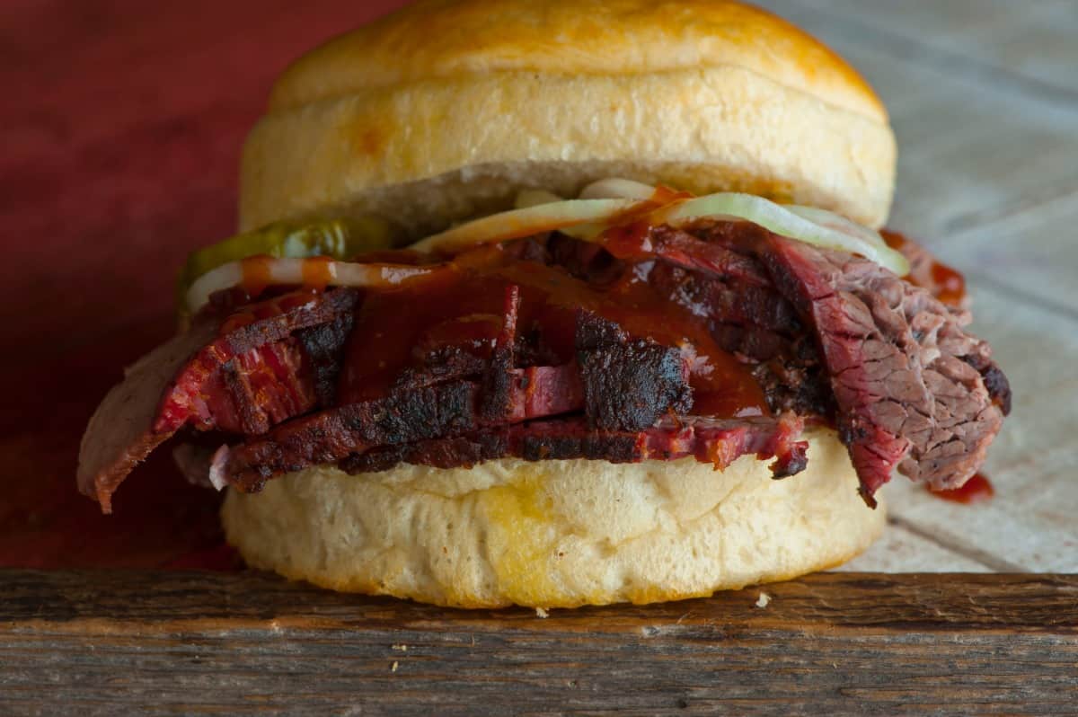 A brisket roll, with sauce and pickles on top of the sliced brisket
