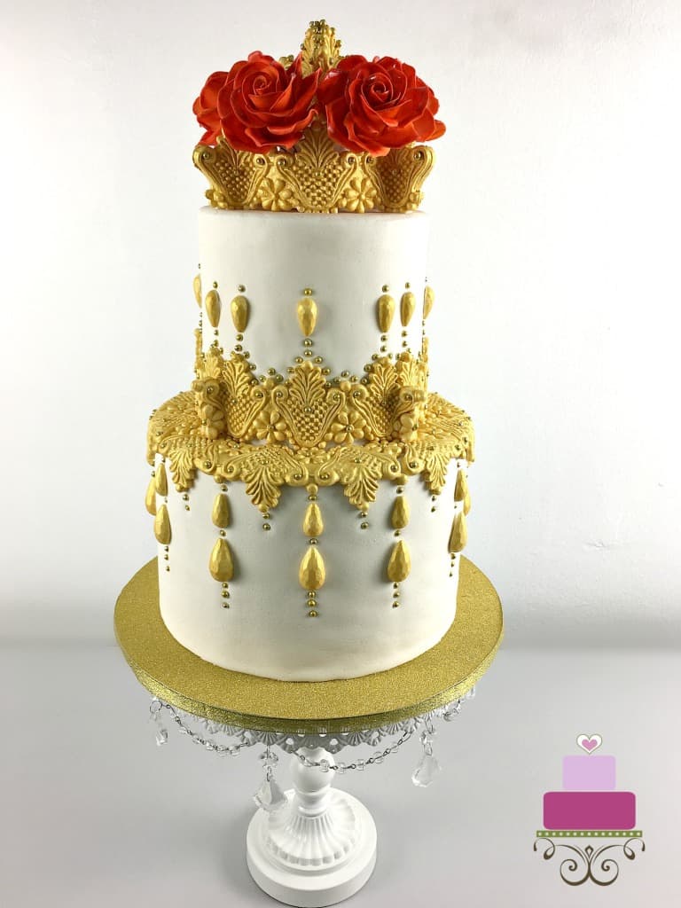 A two-tiered cake decorated with golden lace and red roses