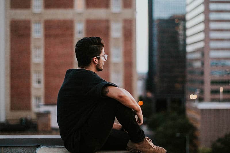 man sitting on roof and looking at city