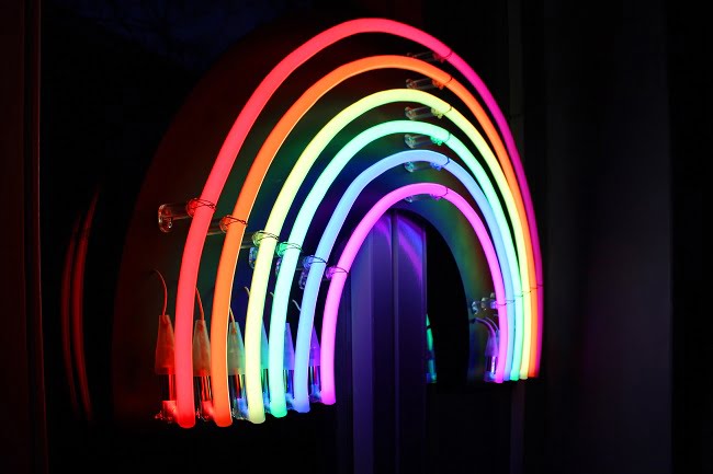 A neon rainbow lights up a dark wall.