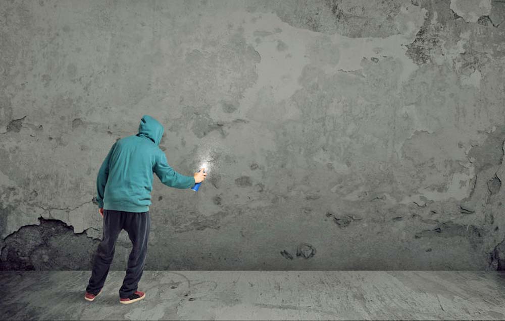 Hooded man spray painting on blank wall