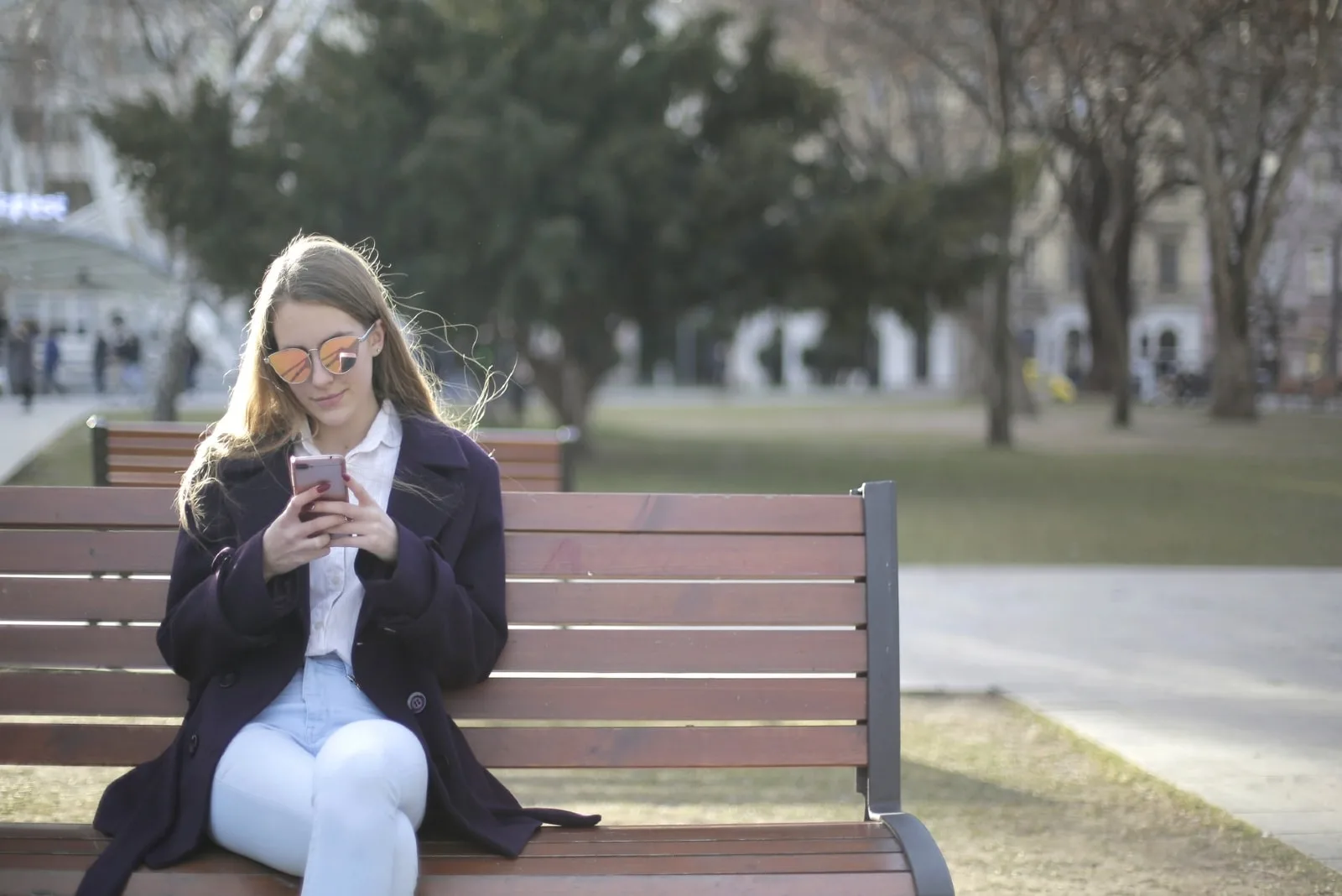 woman with sunglasses using smartphone while sitting on bench