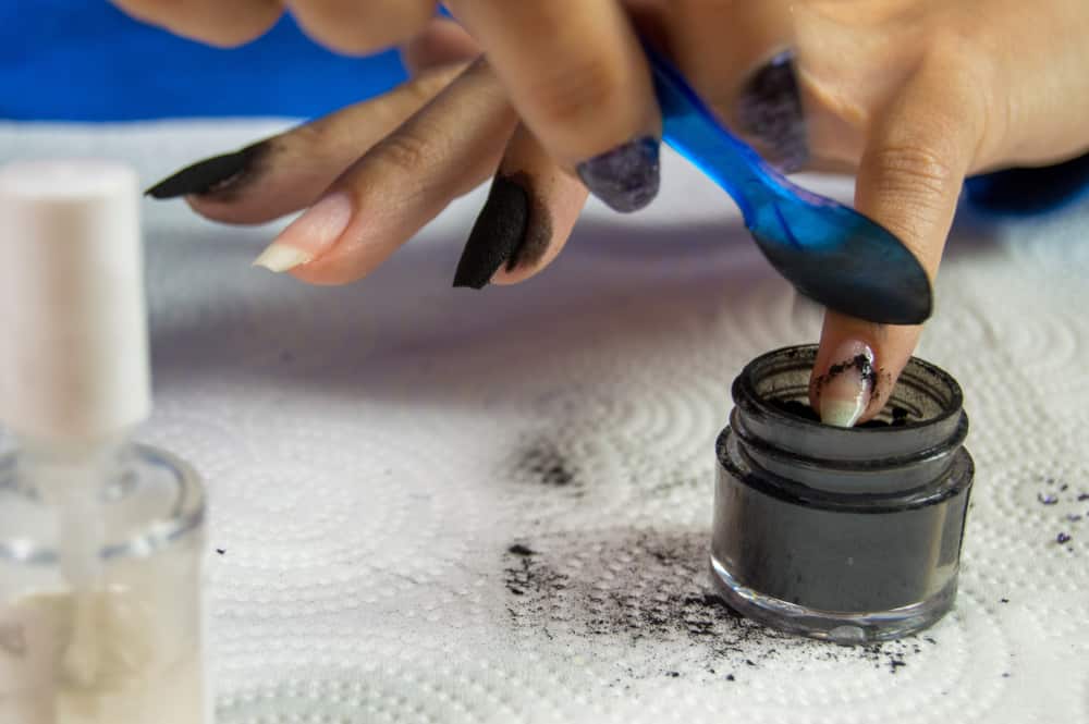 Woman spooning dip powder on to base coat covered fingernail
