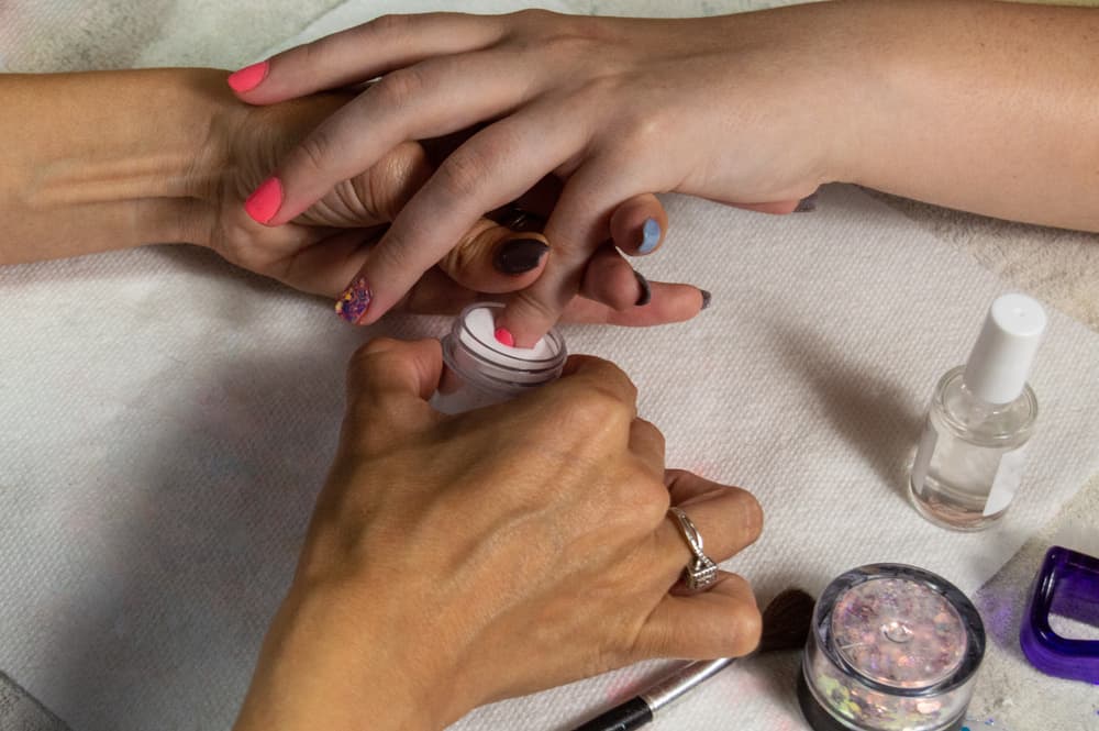Manicurist dipping fingernail into pink acrylic powder