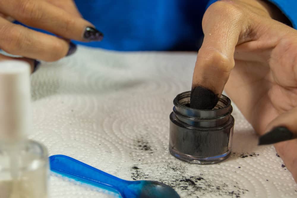 Woman dipping her left thumb in black dip powder