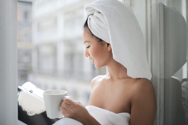 woman with towel on her head reading magazine near window