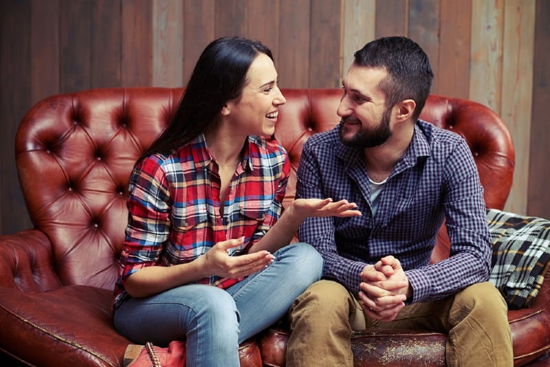 smiling woman talking to man while sitting on couch