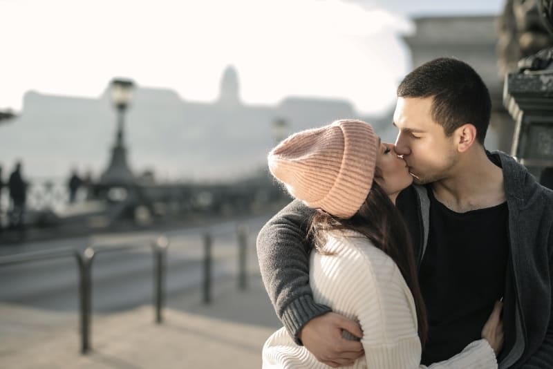 woman with cap and man kissing while standing outdoor