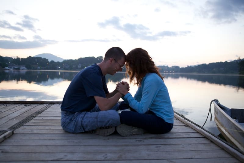 man and woman holding hands while sitting on dock
