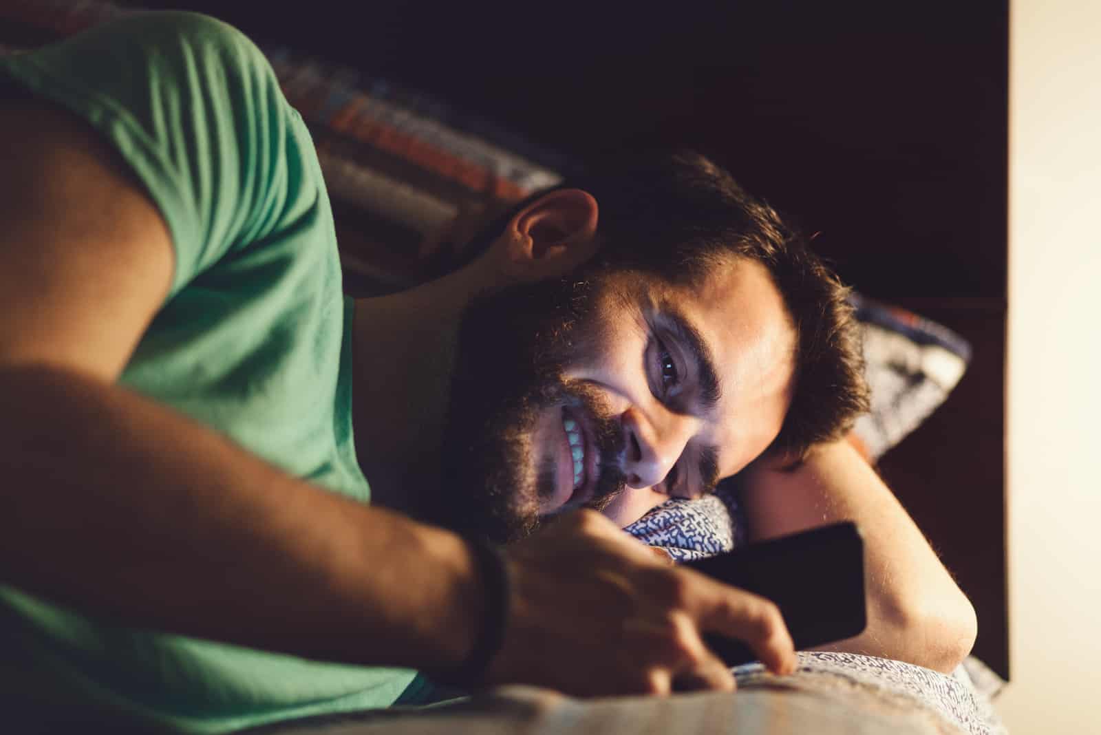 happy man lying on his bed reading messages