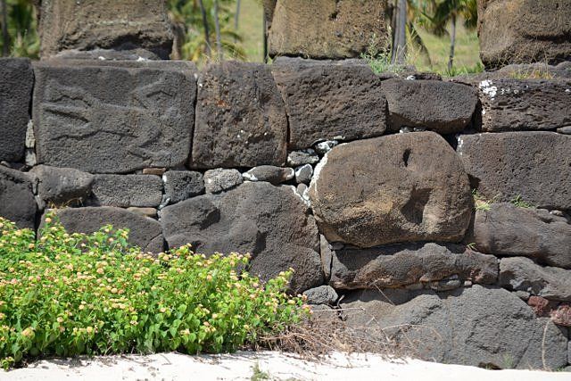 Cabeza reciclada de un moai antiguo y petroglifo con figura mitológica en el muro posterior del Ahu Nau Nau en Isla de Pascua