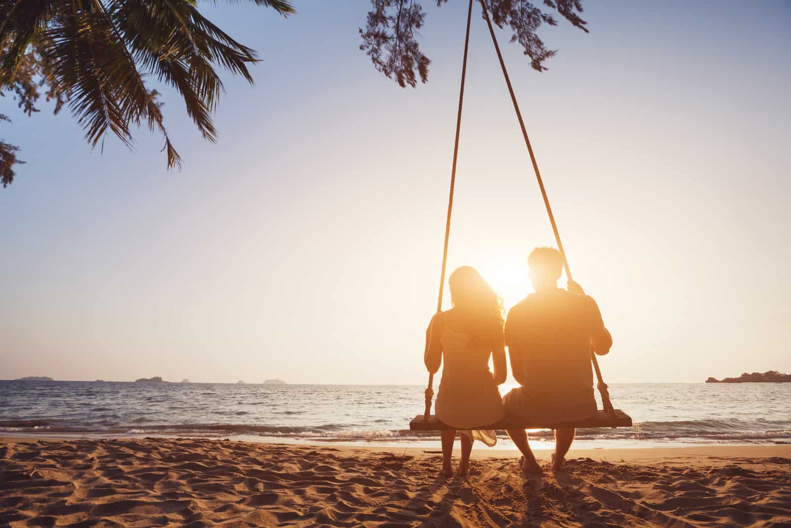 a man and a woman are swinging on a swing next to the beach